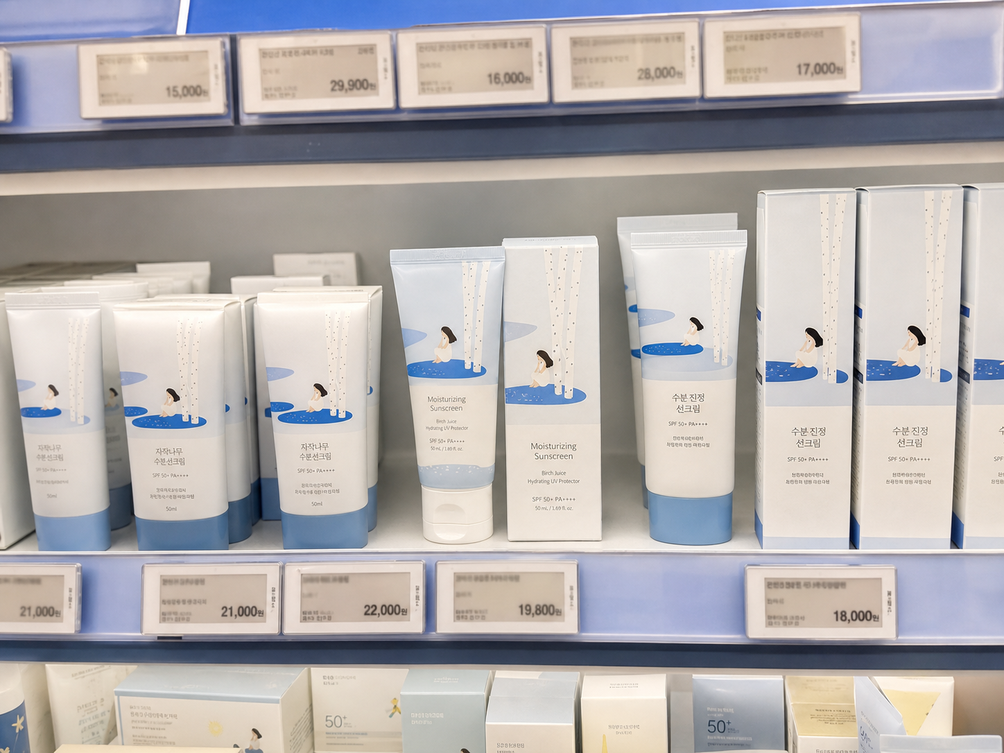 AI-assisted editorial visualization of a generic birch-inspired moisturizing sunscreen in a Korean beauty store · shelf comparison
