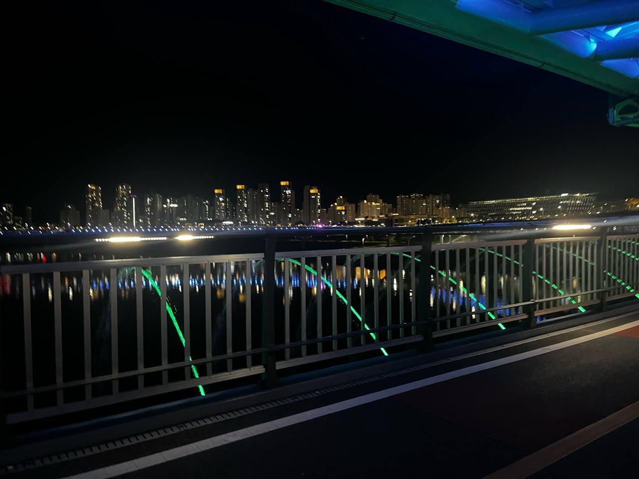 난간 사이 초록 조명의 물줄기와 수면 및 도심 야경