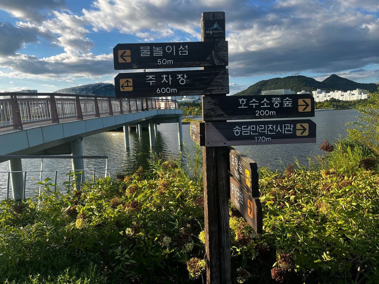 세호교와 호수를 배경으로 물놀이섬과 주차장 방향이 표시된 이정표