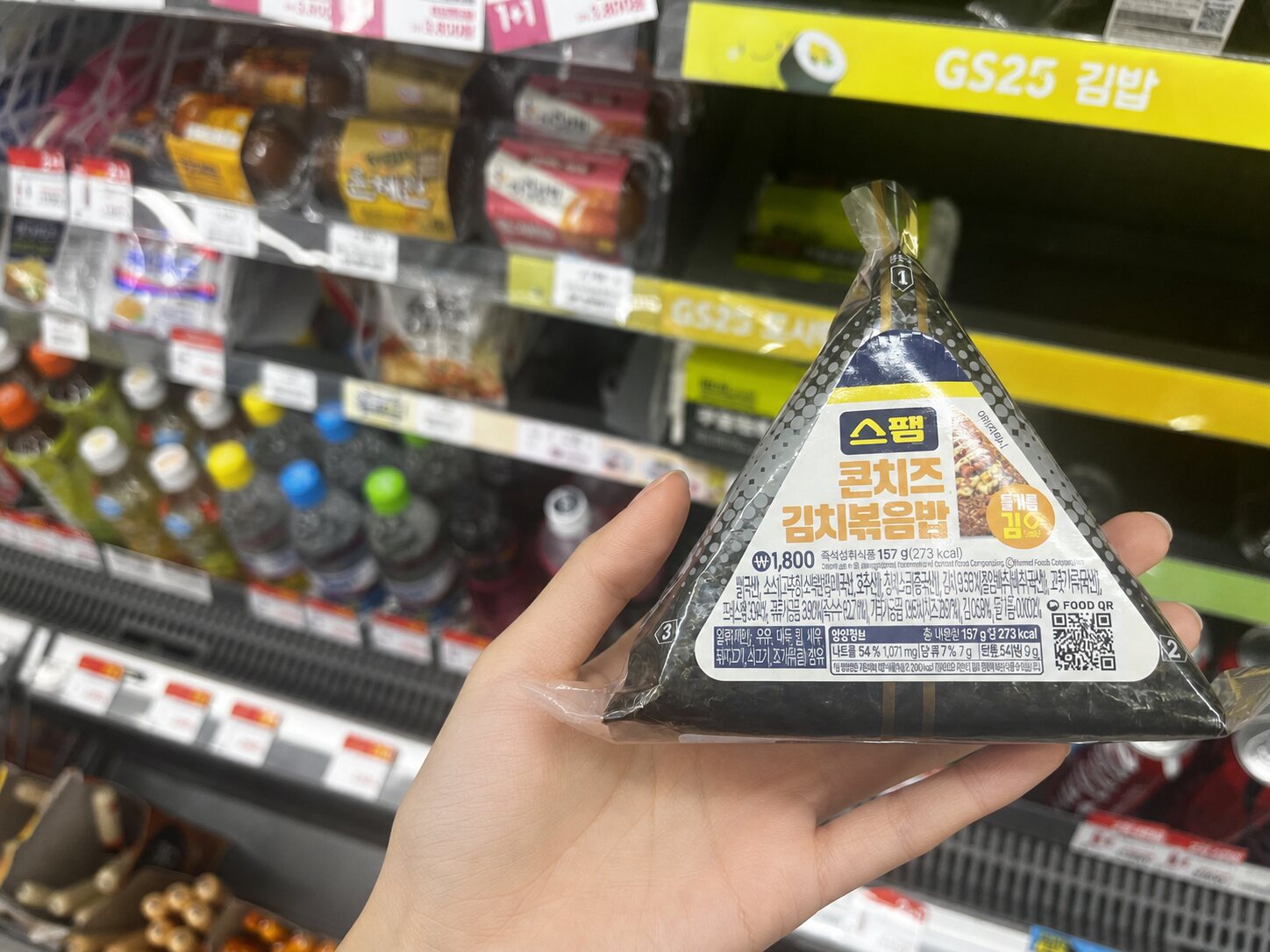 Young adult woman holding Spam corn cheese kimchi fried rice samgak gimbap in a Korean convenience store