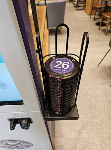 Numbered café vibrating pagers stacked in a charging stand beside a kiosk